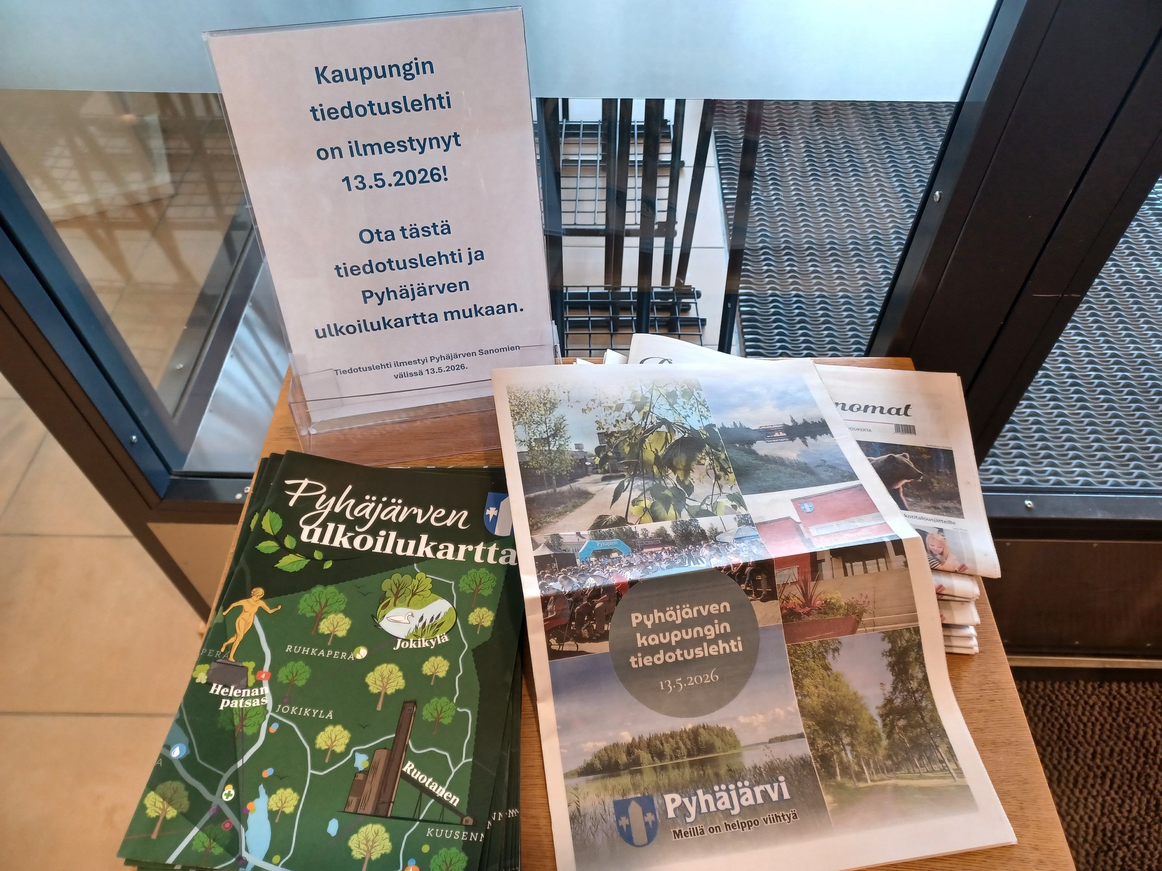 kuvassa on tiedotuslehti ja ulkoilukartta kaupungintalon aulan pöydällä.